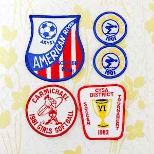 Op de afbeelding: Vier geborduurde patches: een schildvormige American River Soccer 80-81 patch met een voetbal, twee ronde Glen Oaks Swim Team 1981 patches met een zwemmer, een ronde Carmichael 1981 Girls Softball patch en een CYSA District VI Soccer patch.