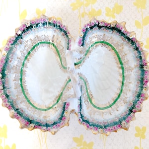 May include: A decorative, double-sided serving dish with a scalloped edge. The dish features a white interior with a green and gold border, accented with pink floral details. The dish is approximately 12 inches wide.