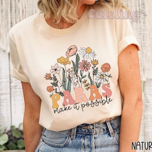 Könnte beinhalten: Ein cremefarbenes T-Shirt mit einem Blumendesign und dem Text "Paras make it possible".