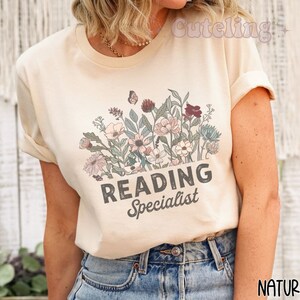 May include: A beige t-shirt with a floral design and the text "Reading Specialist".