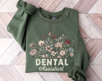 May include: Army green sweatshirt with a floral design and the text "Dental Assistant" in a vintage style font.