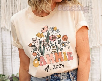 May include: A cream colored t-shirt with a floral design and the text "GAMMIE est. 2024" printed on the front.