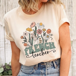 May include: A beige t-shirt with a floral design and the text "French teacher" in green letters.