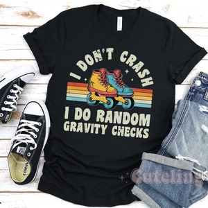 Pu&ograve; includere: Maglietta nera con una grafica retr&ograve; di pattini a rotelle e il testo "I don't crash I do random gravity checks".