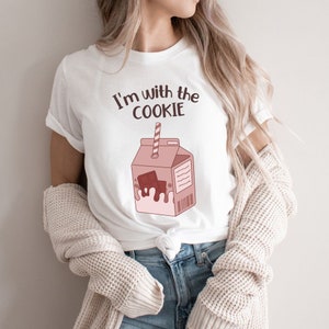 May include: White t-shirt with a brown cartoon illustration of a milk carton with a chocolate bar inside and the text "I'm with the cookie".