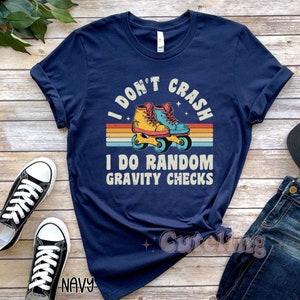 Pu&ograve; includere: Maglietta blu navy con un design arcobaleno retr&ograve; e pattini a rotelle. Il testo sulla maglietta recita "I don't crash I do random gravity checks".