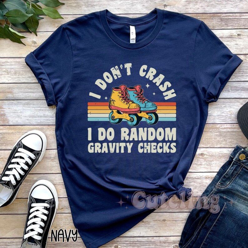 Pu&ograve; includere: Maglietta blu navy con un design arcobaleno retr&ograve; e pattini a rotelle. Il testo sulla maglietta recita "I don't crash I do random gravity checks".
