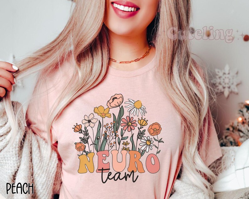 Puede incluir: Una camiseta rosa con un dise&ntilde;o floral y el texto "NEURO team" en letras de colores.