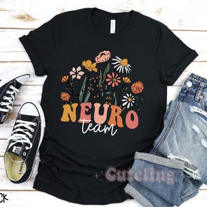 Puede incluir: Camiseta negra con un dise&ntilde;o floral y el texto "Neuro Team" en una fuente retro.