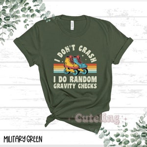 Pu&ograve; includere: Maglietta verde con un design retr&ograve; che presenta un paio di pattini a rotelle e il testo "I don't crash I do random gravity checks".