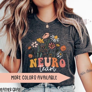 Puede incluir: Camiseta gris oscuro jaspeada con un dise&ntilde;o floral y el texto "Neuro team" en letras de colores. La camiseta est&aacute; disponible en otros colores.