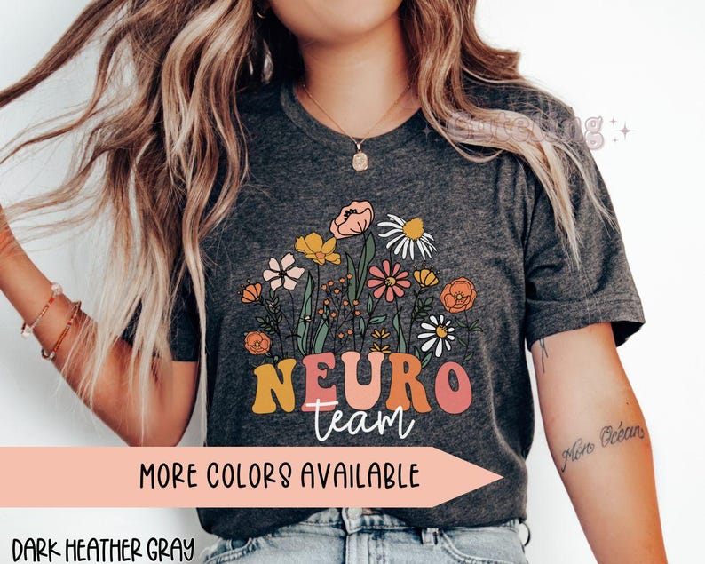 Puede incluir: Camiseta gris oscuro jaspeada con un dise&ntilde;o floral y el texto "Neuro team" en letras de colores. La camiseta est&aacute; disponible en otros colores.