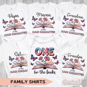 May include: White family shirts with colorful floral and butterfly designs. Each shirt has a different family member's title: Papa, Mama, Grandma, Sister, Grandpa, and a onesie with "ONE". The shirts have the text "of the MAIN CHARACTER" and "for the books".