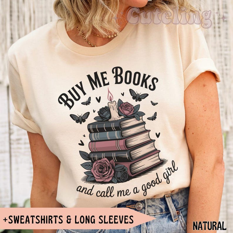 May include: Cream-colored t-shirt with the text "BUY ME BOOKS and call me a good girl." The graphic features a stack of books, roses, butterflies, and a candle. The shirt is labeled "+SWEATSHIRTS & LONG SLEEVES" and "NATURAL".