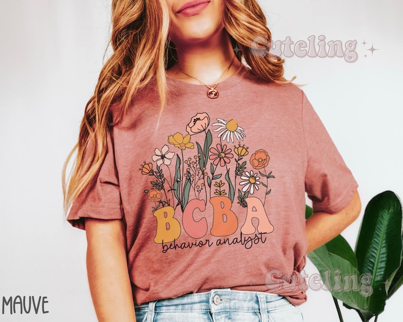 Pu&ograve; includere: Maglietta color malva con un motivo floreale e il testo "BCBA behavior analyst".