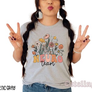 Puede incluir: Una camiseta gris con un dise&ntilde;o floral y el texto "Neuro Team" en una fuente retro.