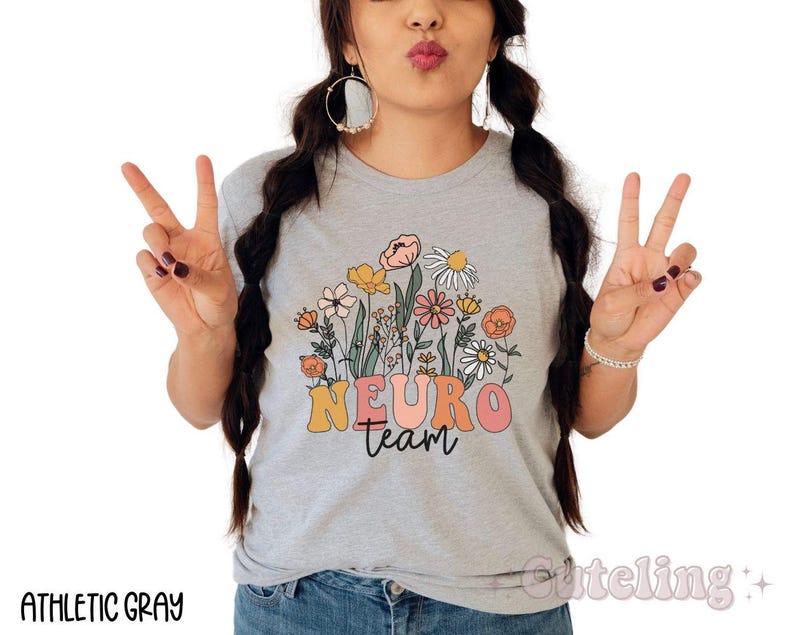Puede incluir: Una camiseta gris con un dise&ntilde;o floral y el texto "Neuro Team" en una fuente retro.