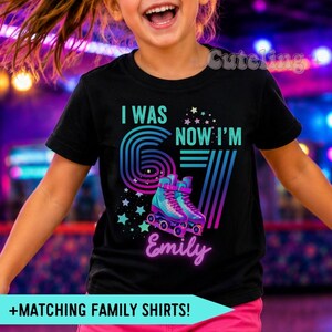 May include: A black t-shirt featuring a graphic with the text I WAS 6 NOW I'M 7. The design includes a large number 6 with a retro striped pattern, a pair of teal and purple roller skates, colorful stars, and the name Emily in script font.