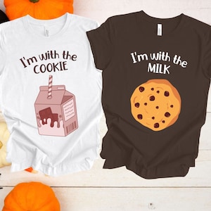 May include: Two white t-shirts with the text "I'm with the cookie" and a cartoon milk carton with a chocolate bar inside and "I'm with the milk" and a cartoon chocolate chip cookie.