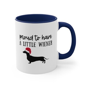 May include: White ceramic mug with a navy blue interior and handle. The mug features the text "proud to have a LITTLE WIENER" above a black dachshund wearing a red Santa hat. A fun, festive design.
