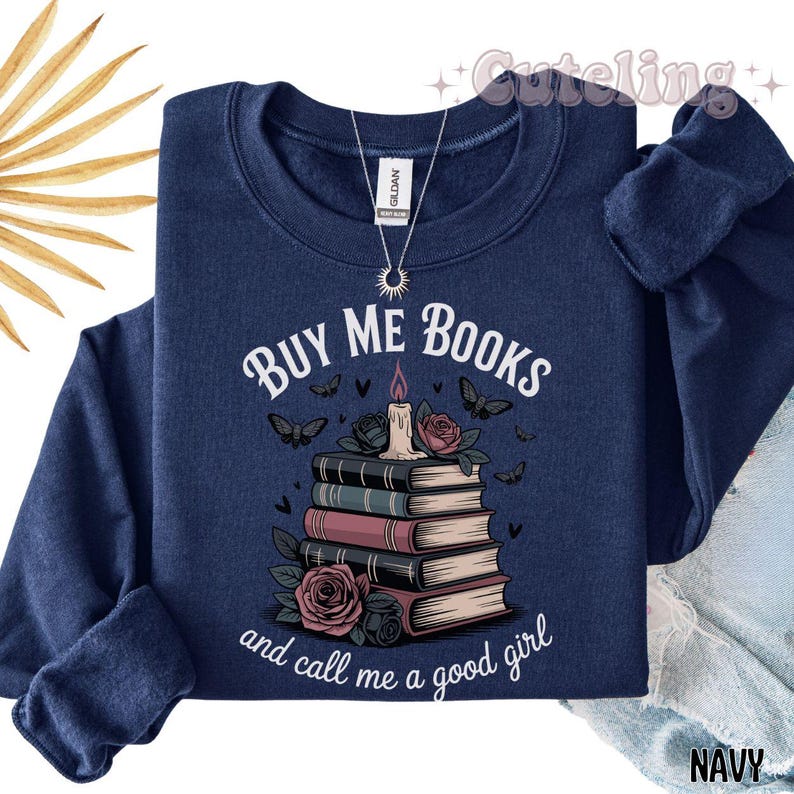 May include: Navy blue sweatshirt with the text "BUY ME BOOKS" above a stack of books, a candle, and roses. The phrase "and call me a good girl" is printed below the books. The sweatshirt has long sleeves.