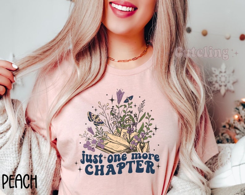 Puede incluir: Una camiseta rosa con un dise&ntilde;o floral y el texto "just one more chapter" en una fuente retro.