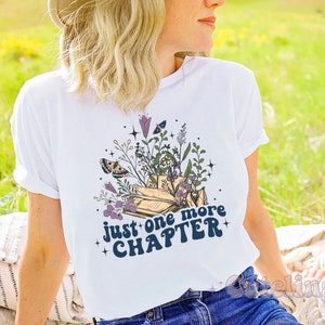 Puede incluir: Camiseta blanca con un dise&ntilde;o floral y el texto "Just one more chapter" en azul.