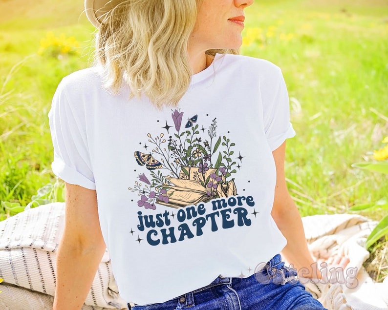 Puede incluir: Camiseta blanca con un dise&ntilde;o floral y el texto "Just one more chapter" en azul.