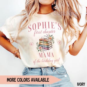 May include: Ivory-colored t-shirt with the text "SOPHIE'S first chapter" in pink script. Below the text is a stack of books with floral accents. The shirt also says "MAMA of the birthday girl".