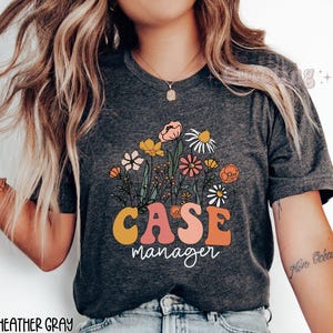 May include: Dark heather gray t-shirt with a floral design and the text "CASE manager" in a retro style.