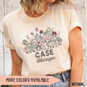 May include: A natural-colored t-shirt featuring a floral design with a butterfly and the text "CASE Manager" in a vintage font. The shirt also has the text "MORE COLORS AVAILABLE" and "NATURAL".
