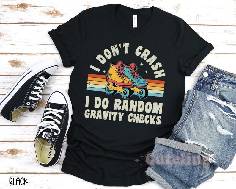 Pu&ograve; includere: Maglietta nera con una grafica retr&ograve; di pattini a rotelle e il testo "I don't crash I do random gravity checks".