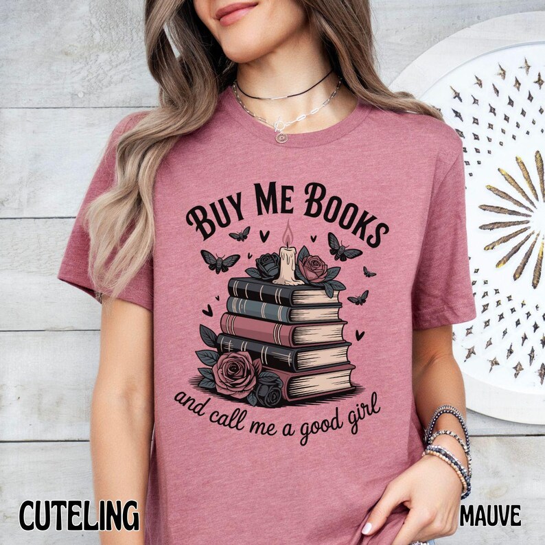 May include: Mauve-colored t-shirt with the text "BUY ME BOOKS and call me a good girl." The graphic features a stack of books, a candle, roses, and butterflies. The word "CUTELING" is printed at the bottom left.