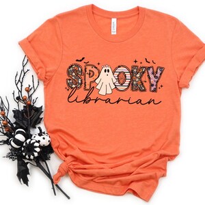 May include: Orange short-sleeved t-shirt with a graphic design of a ghost and the text "Spooky Librarian" in a patchwork style.