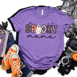 May include: Purple t-shirt with a spooky mama graphic featuring a ghost and the words "Spooky Mama" in a patchwork style.
