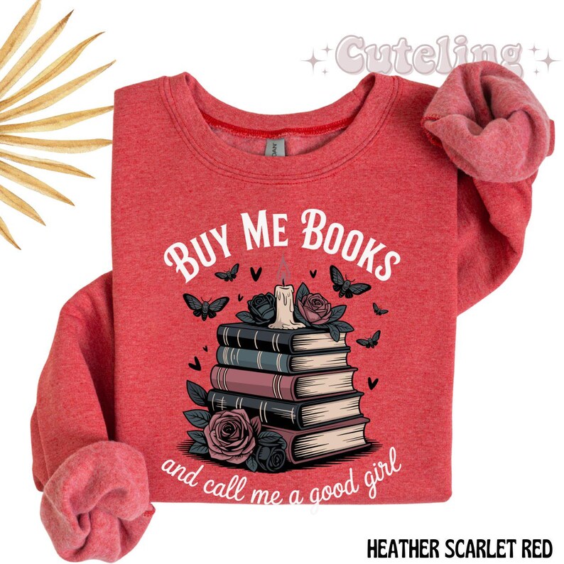 May include: Heather scarlet red sweatshirt with the text "BUY ME BOOKS and call me a good girl". The graphic features a stack of books, roses, butterflies, and a candle.