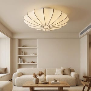 Peut inclure: Un plafonnier rond en tissu blanc cassé avec une forme plissée rappelant une citrouille. Le luminaire présente un moyeu central circulaire d'où rayonnent de fines nervures sombres, créant un aspect segmenté en forme de dôme au plafond.