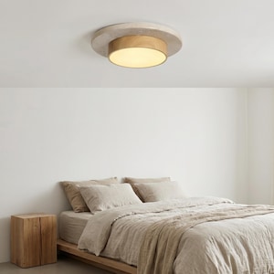 May include: A circular flush mount ceiling light featuring a textured, light grey concrete outer ring and a smooth, light-toned wooden inner band surrounding a central, frosted white glass diffuser that emits a soft, warm glow.