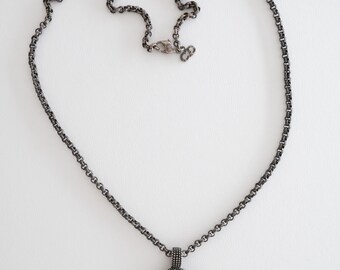 May include: A gunmetal-toned necklace with a floral pendant. The pendant features a rose design with small, sparkling stones and a central clear stone. The chain is a linked design with a lobster clasp.