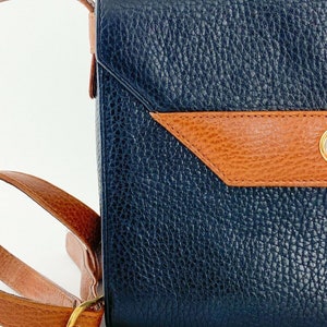 May include: A dark blue leather shoulder bag with a brown leather flap and a gold buckle. The bag has a textured surface.