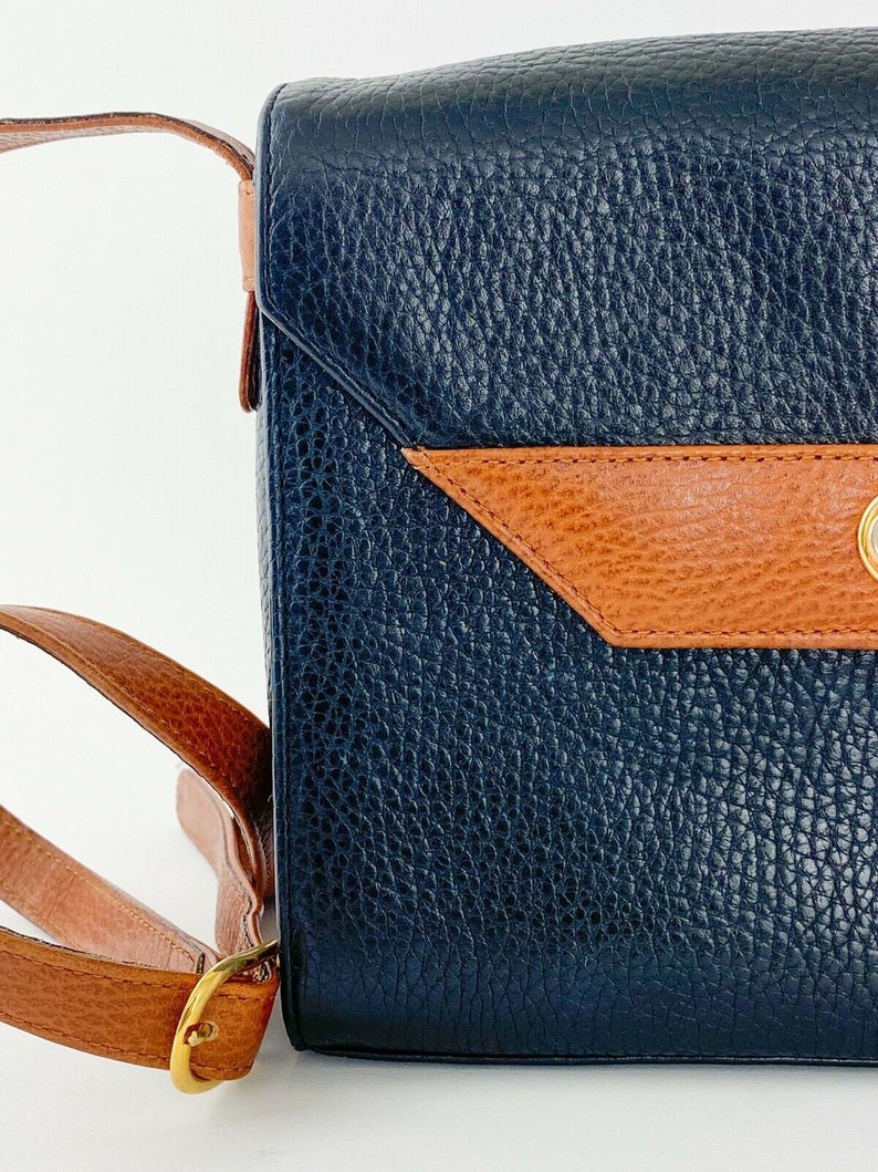 May include: A dark blue leather shoulder bag with a brown leather flap and a gold buckle. The bag has a textured surface.