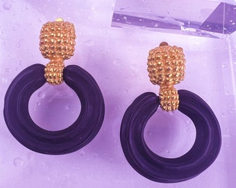 May include: A pair of black and gold earrings with a circular design. The earrings have a textured gold top and a black circular base.