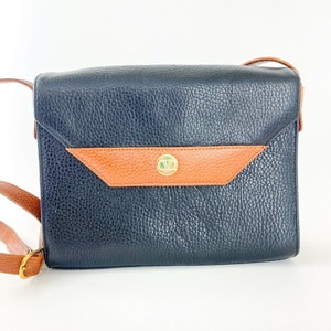 May include: A black leather shoulder bag with a brown leather flap and a gold metal clasp. The bag has a textured surface and a long adjustable strap.