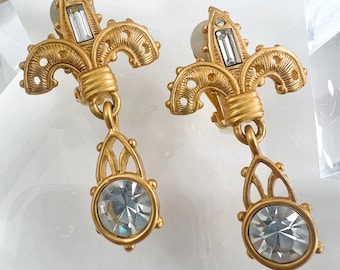 May include: A pair of gold-tone clip-on earrings with a fleur-de-lis design and dangling crystal stones.