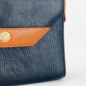 May include: A black leather shoulder bag with a brown leather flap and a gold metal logo. The bag has a textured finish.
