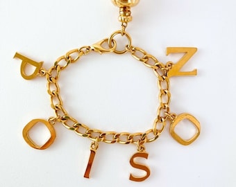 May include: Gold charm bracelet with a gold charm that says "Poison" and letter charms that spell out "Poison".