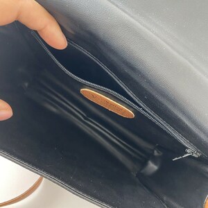 May include: The inside of a black leather purse with a brown leather strap. The purse has a zippered pocket and a brown leather label.