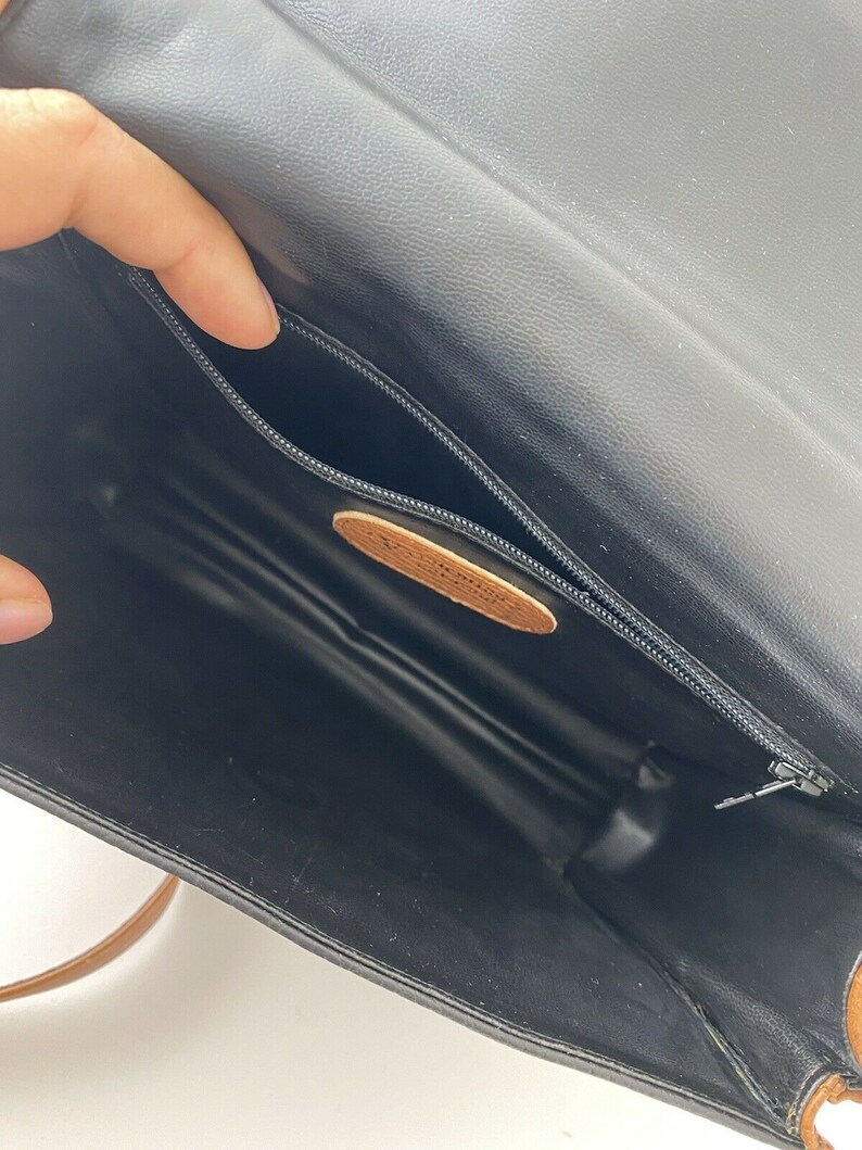 May include: The inside of a black leather purse with a brown leather strap. The purse has a zippered pocket and a brown leather label.