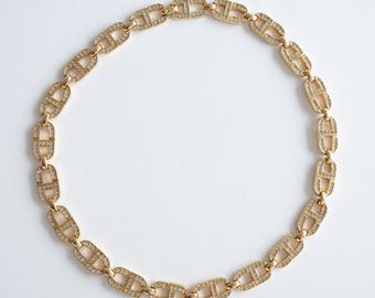 May include: A gold-toned necklace with a repeating link design, each link encrusted with small, sparkling crystals. The necklace is displayed on a white background, highlighting its intricate details and elegant appearance. A piece of jewelry.