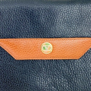 May include: A black leather handbag with a brown leather flap and a gold-toned logo. The bag has a textured surface.